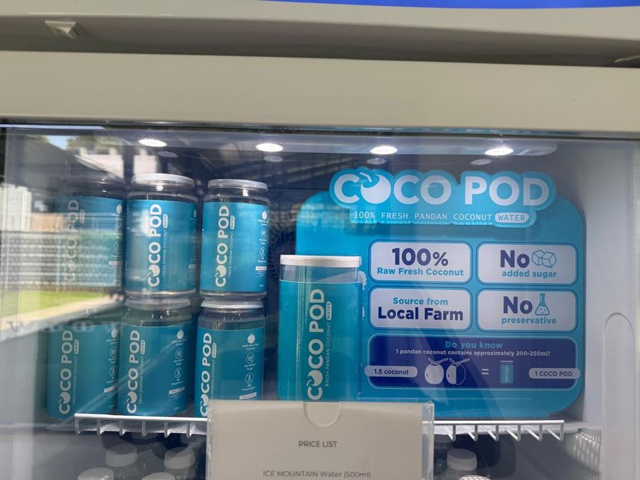 Cocopod pods in a store chiller with a sign: 100% raw fresh coconut, no added sugar, no preservative, sourced from local farm